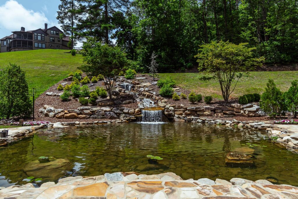 Outdoor pond and rock waterfall with a house on a hill.